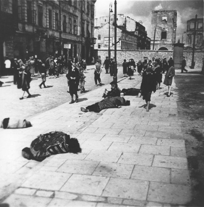 Pedestrians in the Warsaw ghetto walk past corpses lying on the pavement on Rynkowa Street